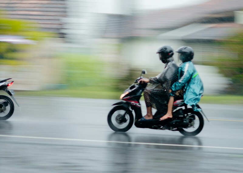 Wisatawan tetap ceria berkendara motor di Jogja saat hujan ringan dengan jas hujan lengkap